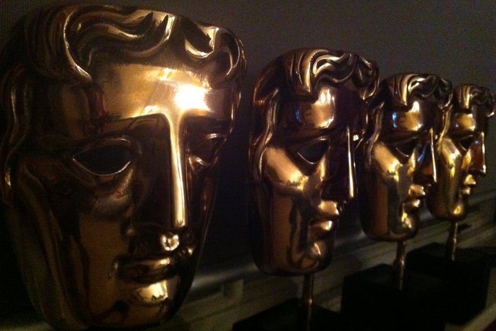 Four shining gold BAFTA awards lined up in dark lighting