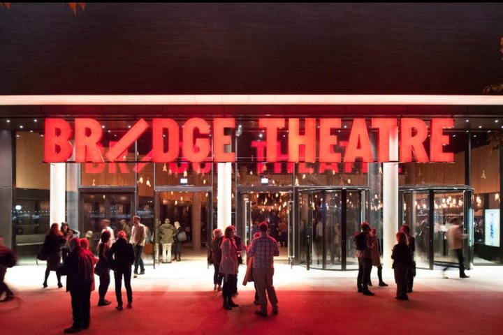 the Bridge Theatre lit up at night with theatregoers outside