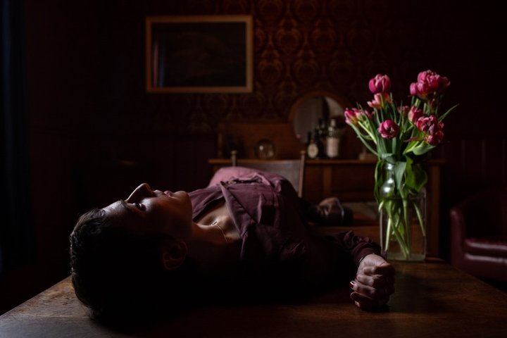 Painterly photograph of woman lying next to flowers from the aspect of the top of her head