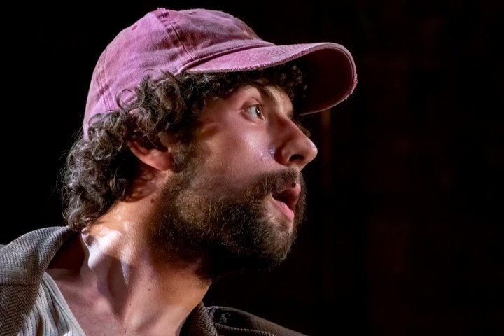 Close up of Keaton's side profile as he looks right in dramatic lighting while wearing a cap.