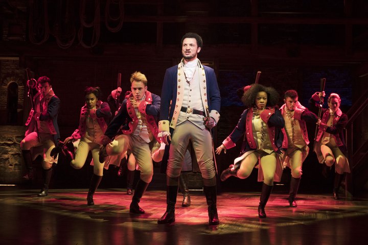 Graduate Jamael Hamilton sings on stage in period costume in the lead role of Alexander Hamilton backed by ensemble dancers