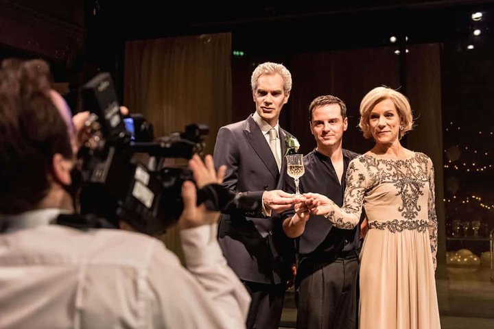 Juliet Stevenson with Andrew Scott and Angus Wright raise a glass of champagne to a camera in a scene from Hamlet