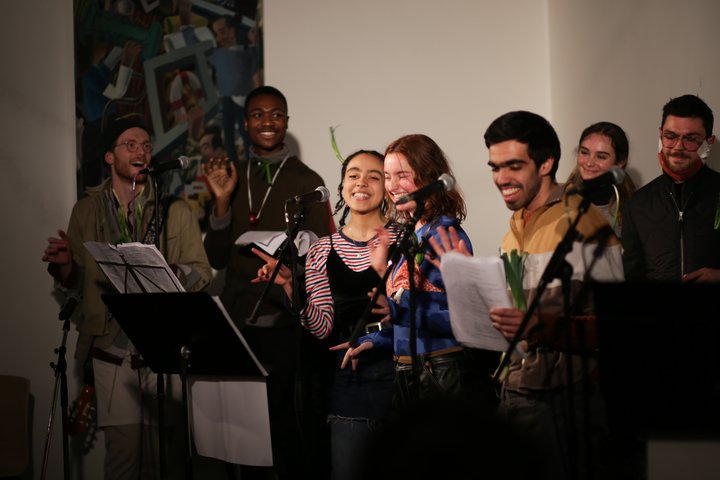 A group of students stand at microphones, laughing and gesturing with animated expressions