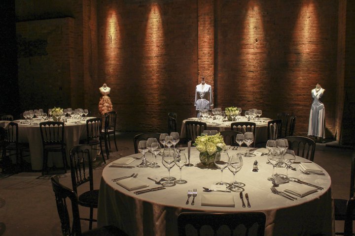 empty round tables set for dinner in the RADA GBS Theatre with costumes on mannequins decorating the room