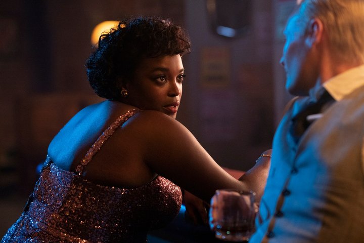 Actress Wunmi Mosaku sits at a bar in a sequinned dress in a scene from TV show Lovecraft Country